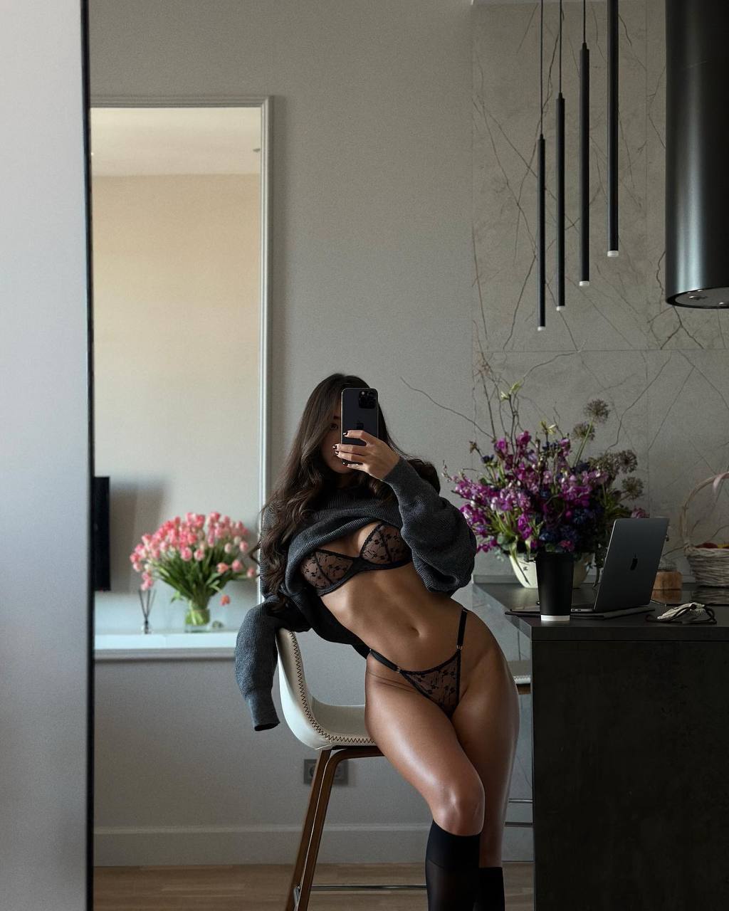 Ultra-realistic luxury lifestyle editorial featuring an elegant brunette woman taking a mirror selfie in designer black lingerie and oversized knit sweater inside a modern minimalist apartment with premium interior, soft natural lighting, sophisticated fashion photography.
