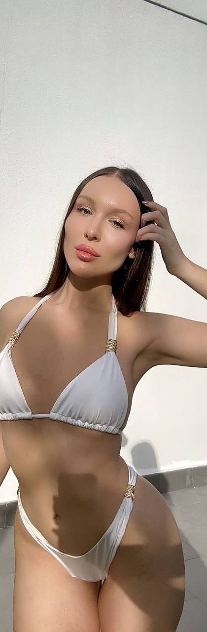 Beautiful brunette fashion model wearing a luxury white bikini with gold accents, posing by a modern villa in bright natural sunlight, elegant resort atmosphere, toned figure, editorial swimwear photography, premium lifestyle aesthetic.