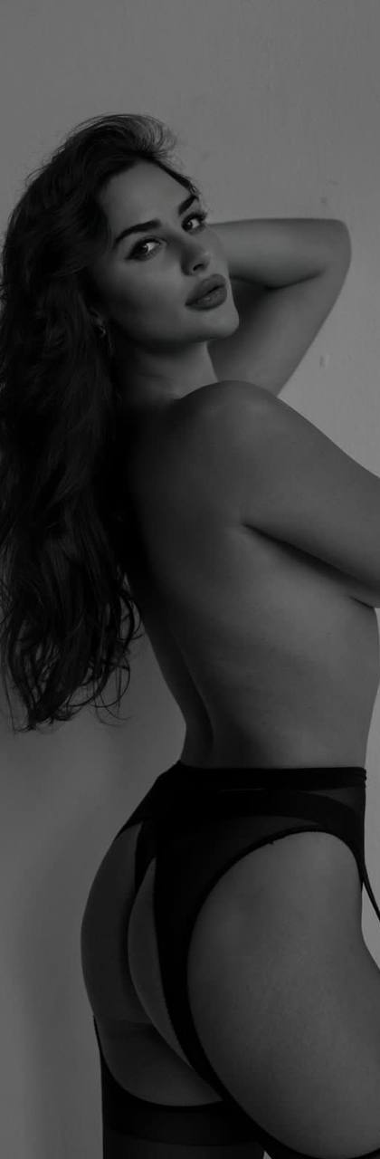 Black and white artistic boudoir portrait of a woman with long wavy hair in a garter belt and stockings posing in profile