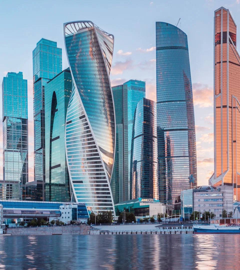 Ultra-realistic architectural cityscape of Moscow International Business Center (Moscow-City) at golden hour, viewed from across the Moscow River. Iconic futuristic glass skyscrapers reflecting warm sunset light, calm water with mirror-like reflections, pastel sky with soft clouds, modern bridges, luxury urban atmosphere, clean composition, ultra-sharp details, cinematic lighting, photorealistic 8K, HDR, premium travel editorial photography, natural colors, high dynamic range, architectural masterpiece, wide-angle perspective, luxury metropolis aesthetic.