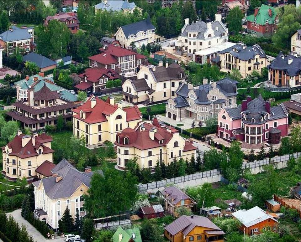 Ultra-realistic aerial view of an exclusive luxury residential neighborhood featuring elegant European-style mansions surrounded by lush greenery. Grand private villas with sophisticated architecture, manicured gardens, tree-lined streets, premium gated estates, landscaped properties, upscale suburban atmosphere, vibrant summer foliage, natural daylight, cinematic drone perspective, harmonious blend of luxury homes and nature, photorealistic 8K, HDR, ultra-detailed textures, premium real estate editorial photography, architectural excellence, affluent residential district, wide-angle aerial composition.